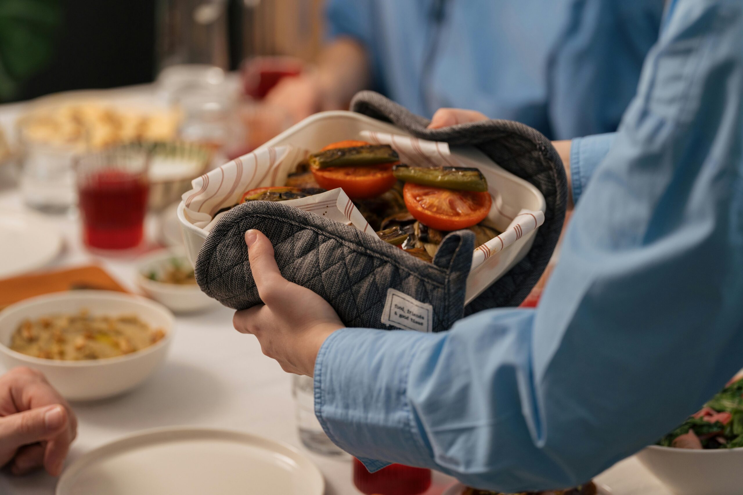 Close-up of hands serving a freshly baked vegetable dish at a dinner table setting.